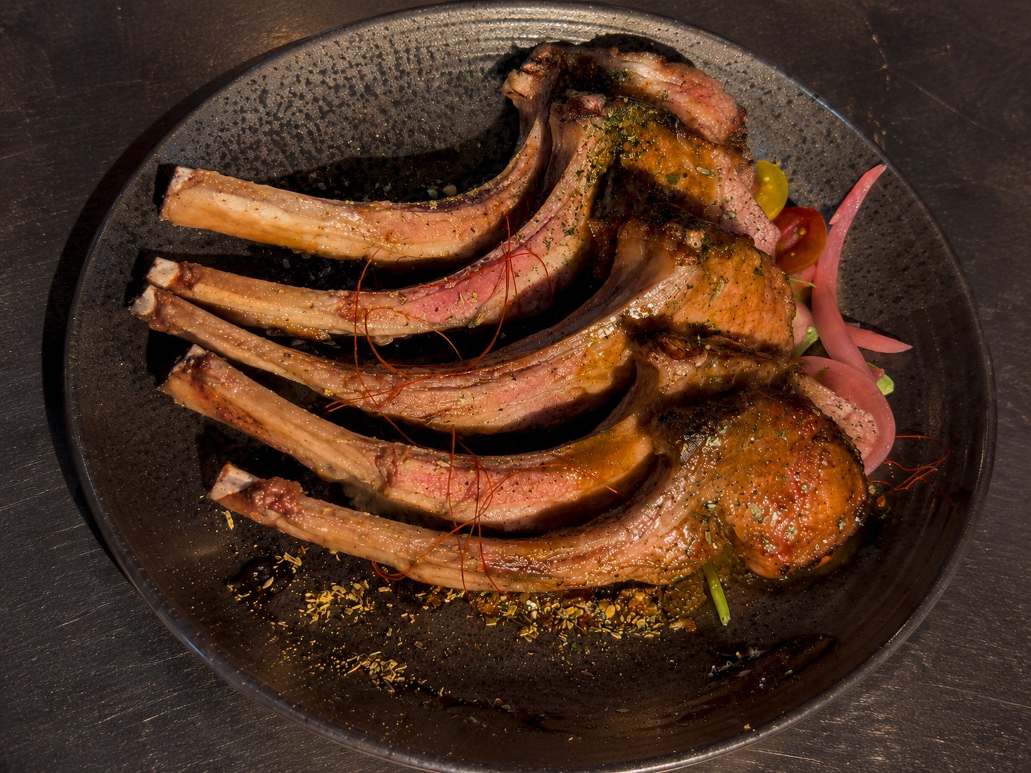 Frenched lamb chops fanned on a dark plate with pickled onions, off the Josper grill at Renzo's St. Pete