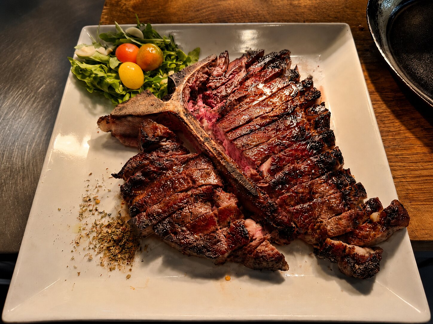 Grilled porterhouse steak, sliced and served on a white plate with an arugula and heirloom-tomato salad at Renzo's St. Pete