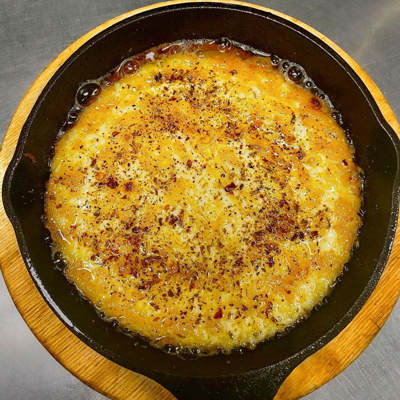 Grilled provoleta bubbling in a cast-iron skillet with Argentine adobo at Renzo's St. Pete