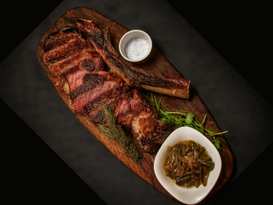 Sliced dry-aged Tomahawk ribeye on a wooden board with sea salt and caramelized onions at Renzo's St. Pete